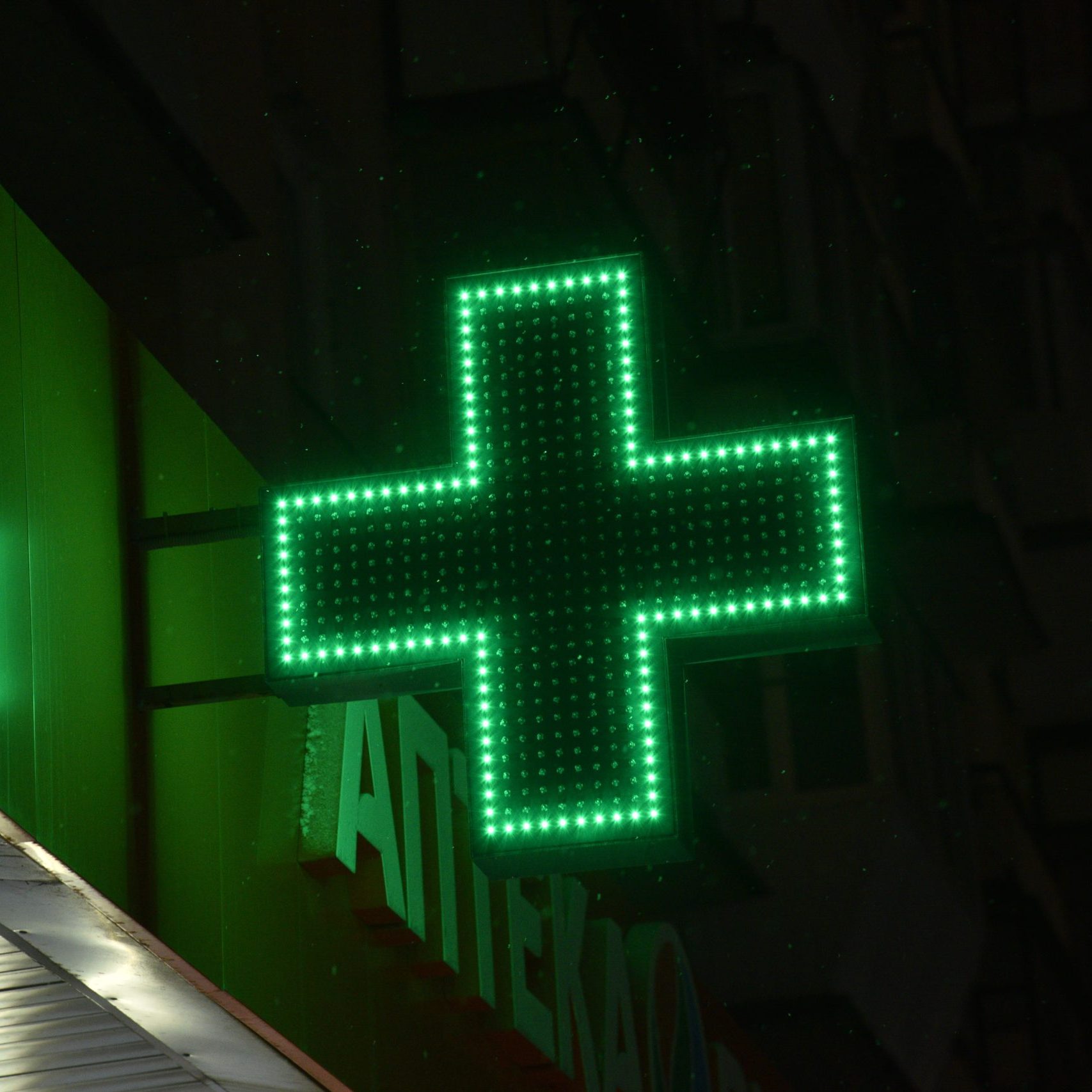 Green cross pharmacies at night in the city. Glowing with LED lamps, the green cross of the hospital.