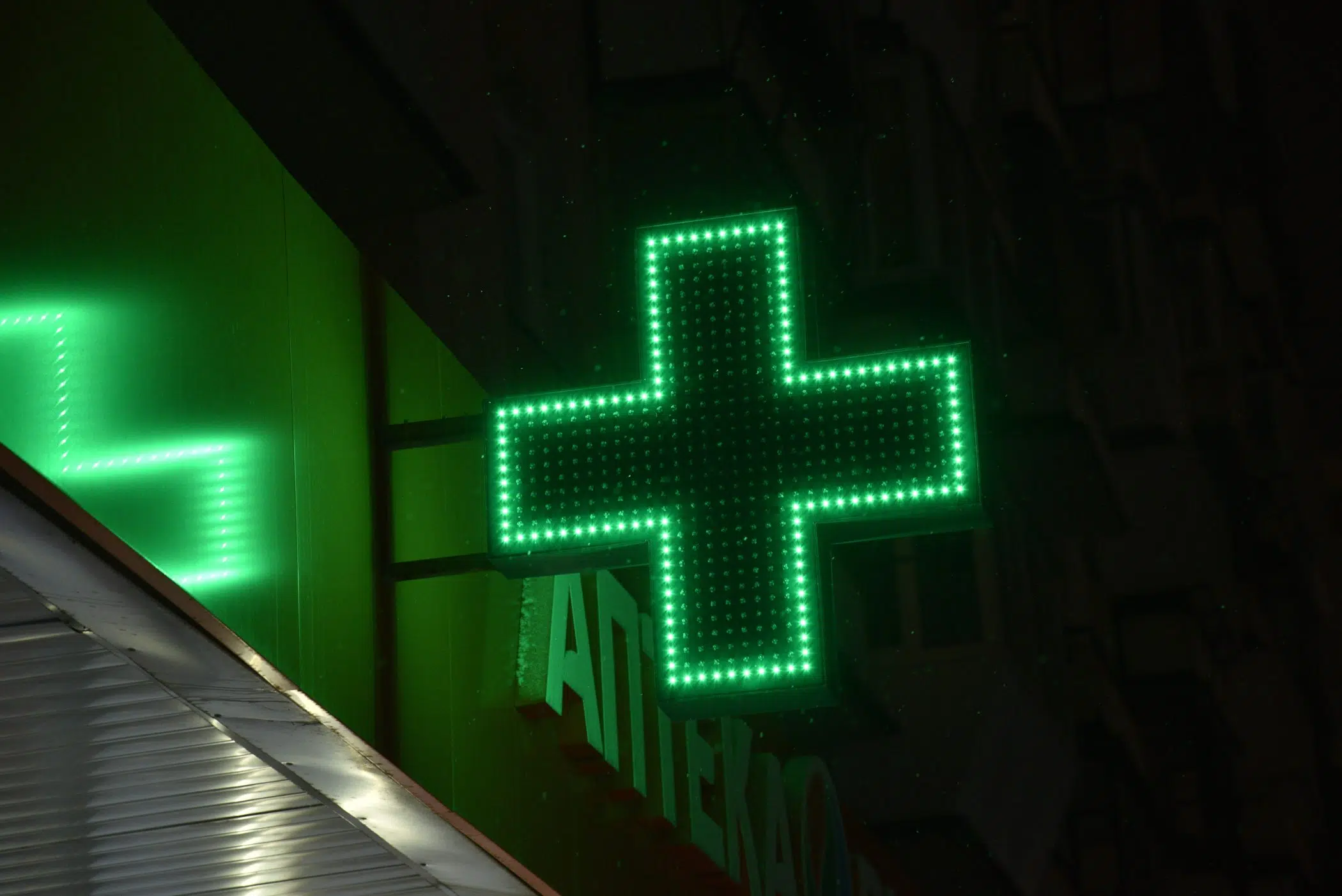 Green cross pharmacies at night in the city. Glowing with LED lamps, the green cross of the hospital.