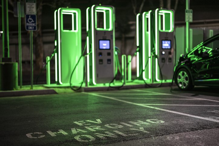 Electric vehicle charging station seen during the night on a public parking with green lights.
