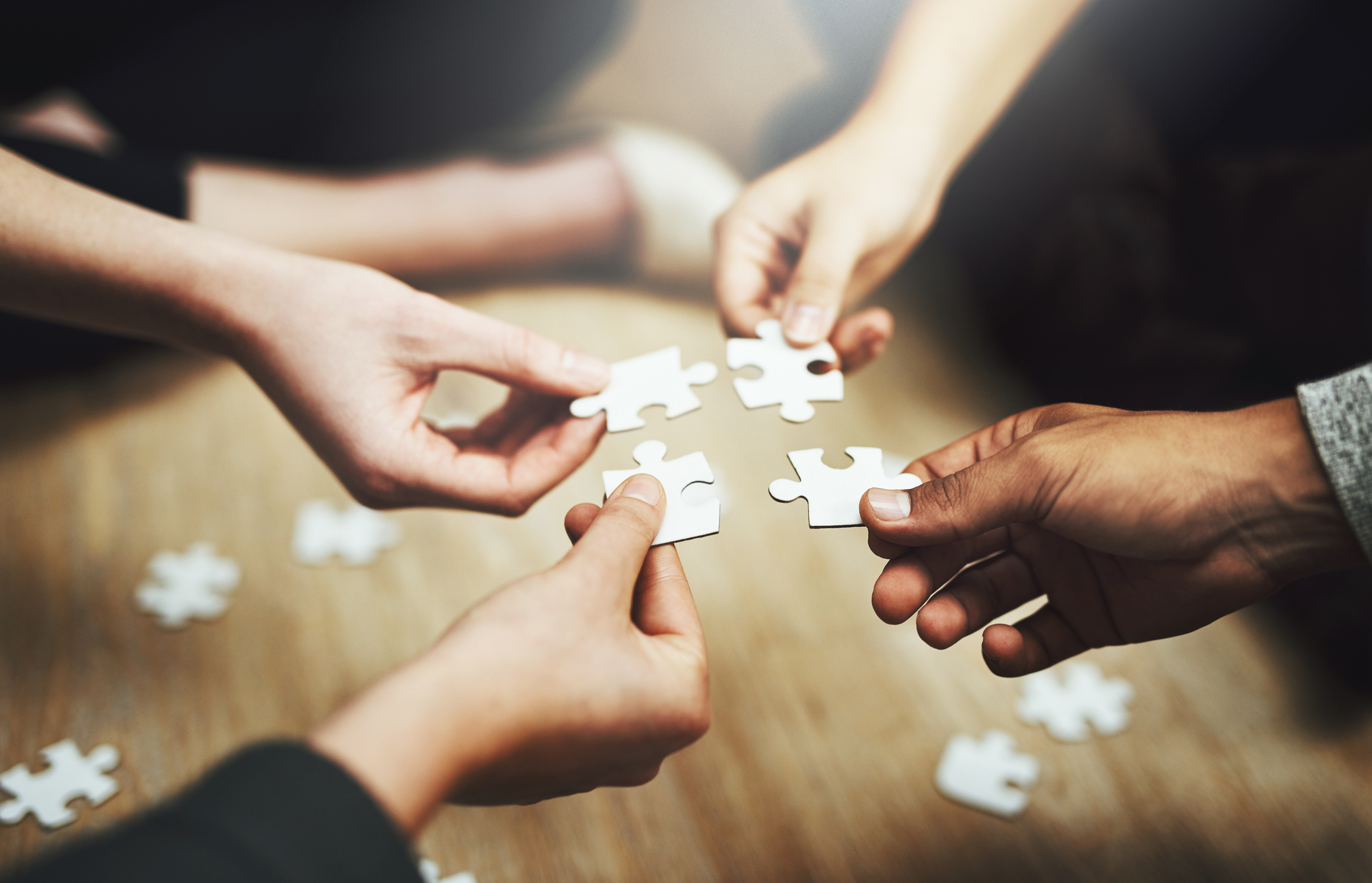 Cropped shot of a group of people fitting puzzle pieces together on the floor